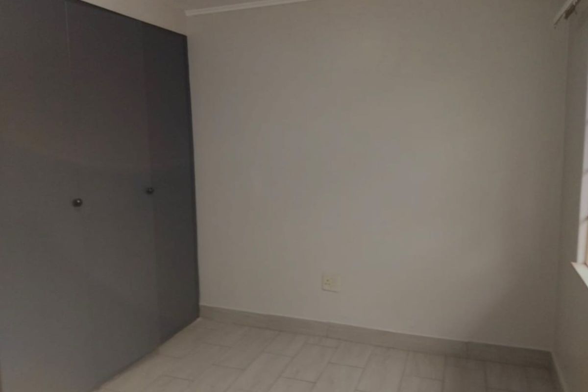 A clean, empty bedroom featuring modern grey built-in cupboards and neutral tiled flooring, providing a versatile space ready for personalization.