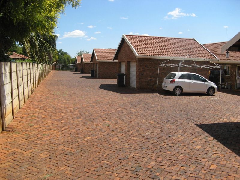 Exterior view of a townhouse complex featuring a paved driveway, multiple garage units with tiled roofs, and a perimeter boundary wall.