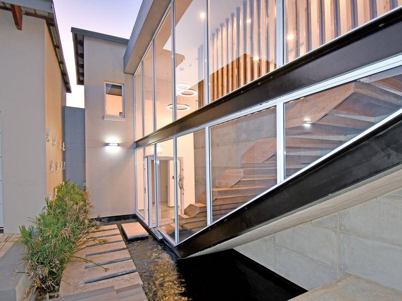 Modern architectural exterior featuring a striking glass facade, steel staircase, and a tranquil water feature with a stone pathway.