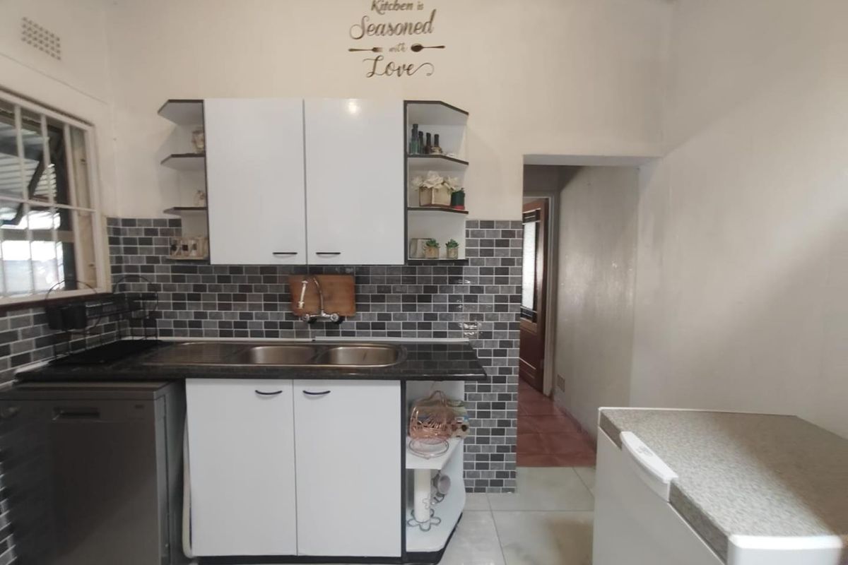 A functional kitchen featuring white cabinetry, a dark countertop, a double stainless steel sink, and a grey mosaic tile backsplash.