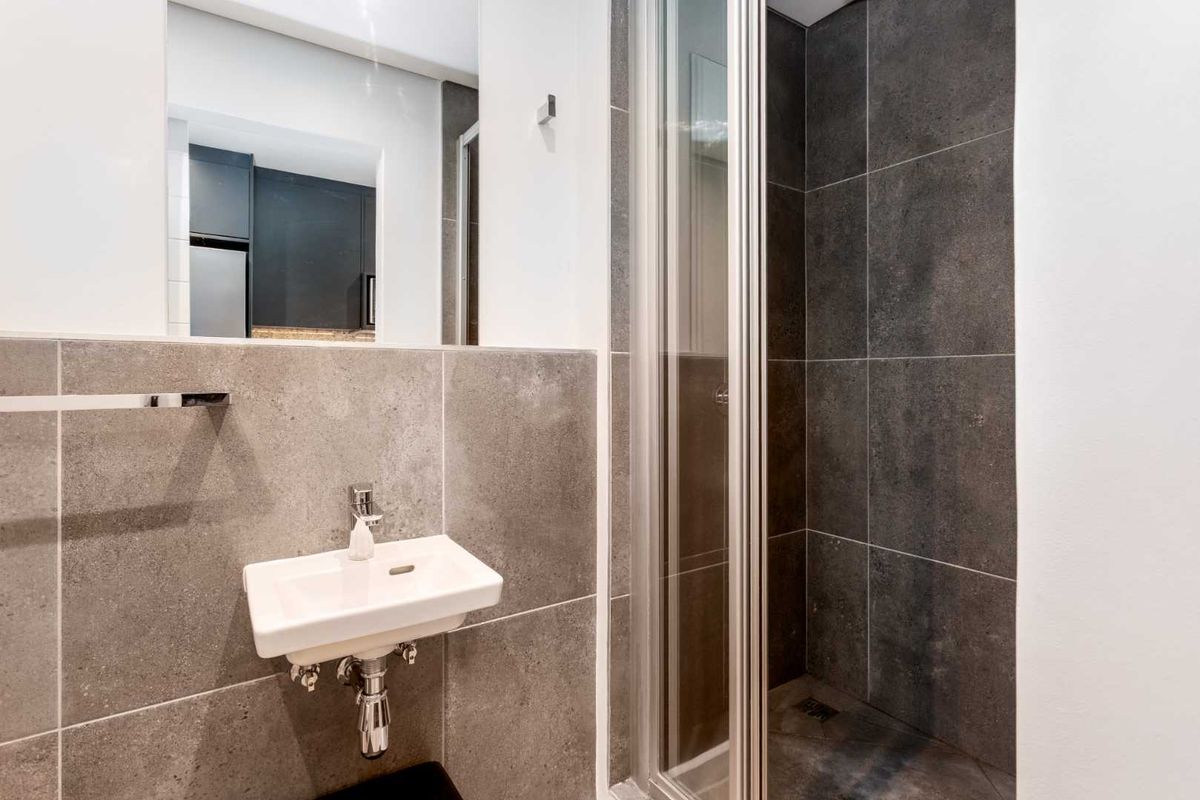 Modern bathroom featuring a wall-mounted basin, chrome fixtures, and a walk-in shower with contemporary grey tiling.