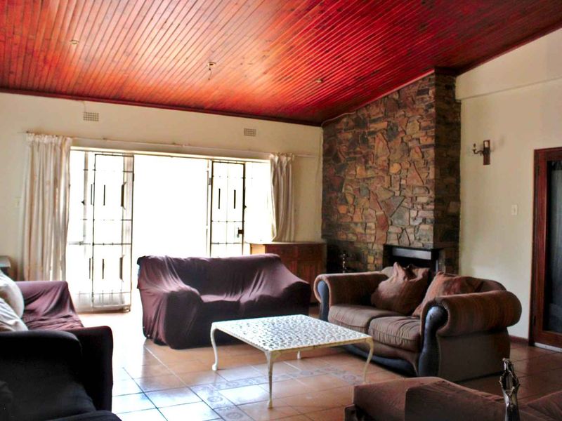 Spacious living room featuring a prominent stone fireplace, tiled flooring, and a distinctive timber tongue and groove ceiling with access to the exterior.