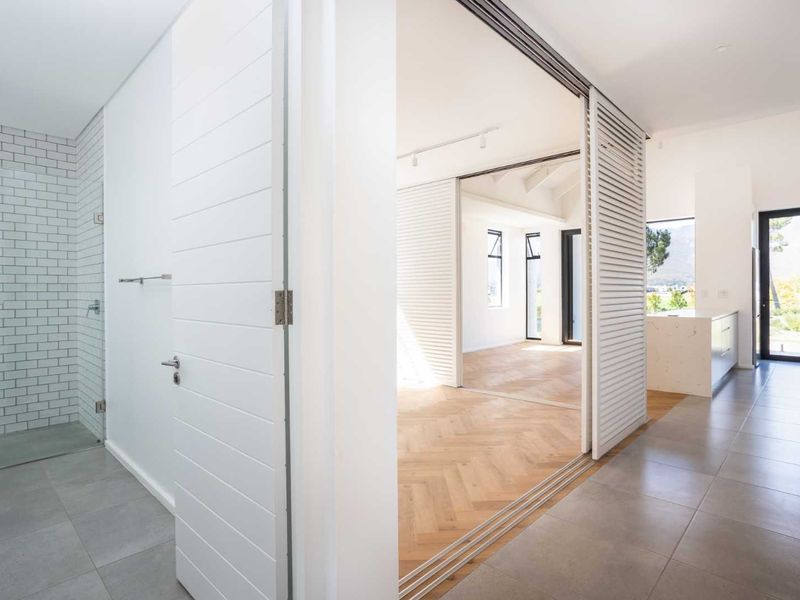 Modern open-plan living area featuring herringbone timber floors, sleek sliding louvered partitions, and a contemporary kitchen with stone island and tiled bathroom.