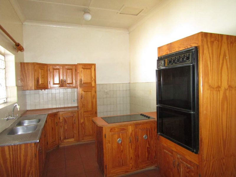 A dated kitchen featuring wooden cabinetry, a built-in double oven, electric hob, and double sink with tiled splashbacks and flooring.