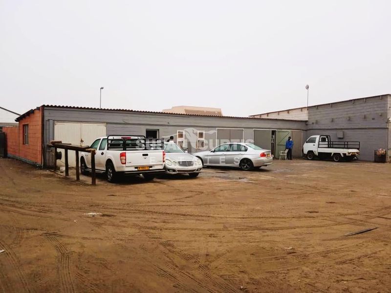 Industrial property exterior featuring multiple roller door access points, concrete block construction, and a large unpaved yard area.