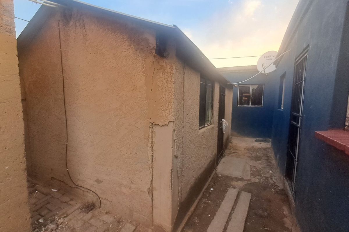 A narrow exterior side passage between two structures showing significant wear to the exterior plaster and paintwork.