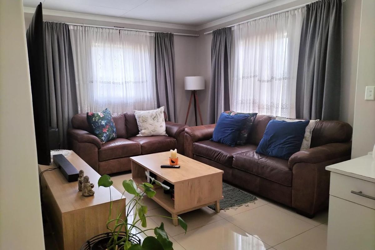 A well-maintained living room featuring neutral tiled flooring, coved ceilings, and dual windows with fitted curtain tracks.