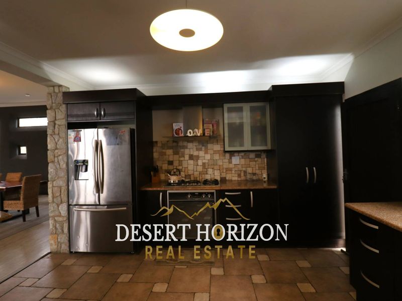 A functional kitchen featuring dark cabinetry, granite countertops, a tiled backsplash, and built-in oven and hob, seamlessly integrated into an open-plan living space.