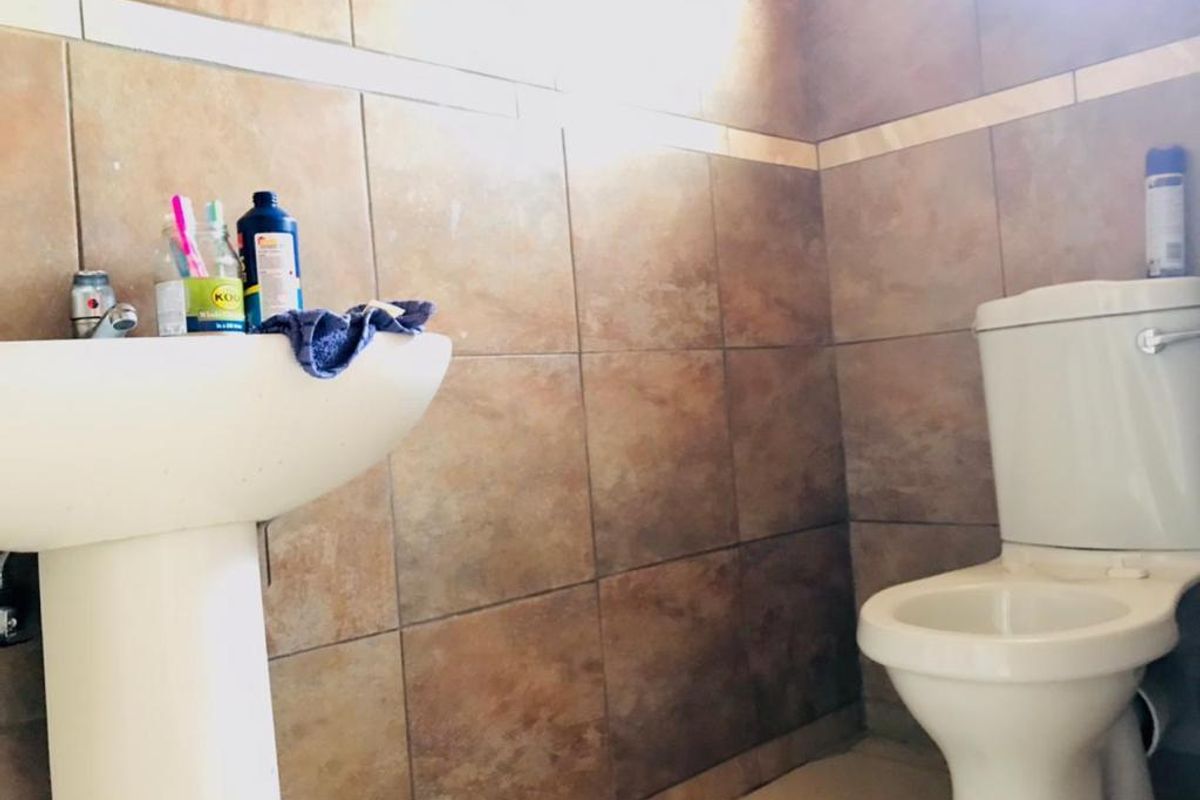 A functional bathroom featuring a pedestal sink and a standard toilet, finished with full-height wall tiling.