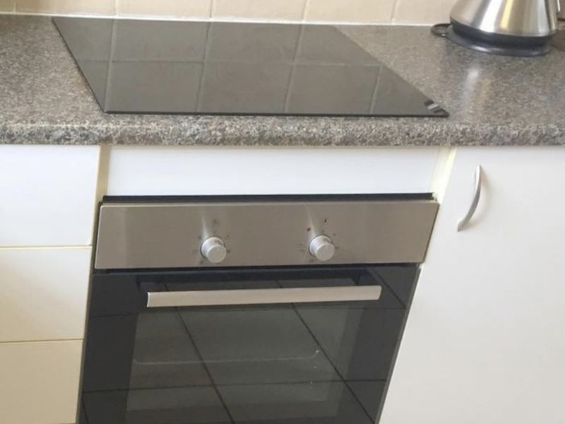 A clean kitchen section featuring a built-in Bosch oven, ceramic hob, neutral laminate countertop, and white cabinetry with a tiled backsplash.