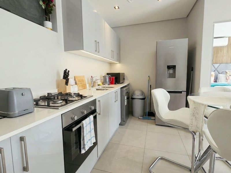 Modern kitchen featuring sleek gloss cabinetry, quartz countertops, a gas hob, and built-in oven, complemented by recessed downlighting and under-cabinet task lighting.