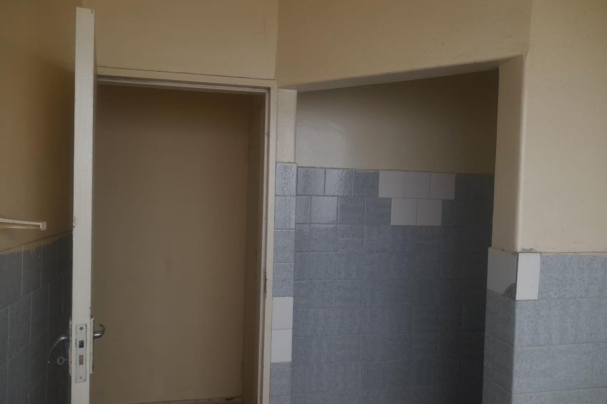 A dated bathroom interior featuring partial wall tiling and a doorway, requiring cosmetic updates and repairs to the wall finishes.