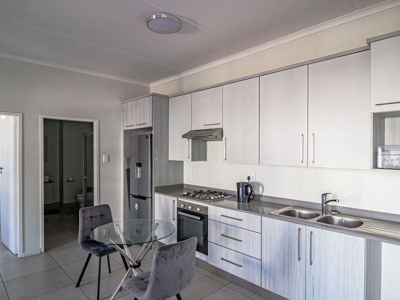 Modern open-plan kitchen featuring light wood-grain cabinetry, gas hob, electric oven, and integrated sink, seamlessly flowing into the living area.