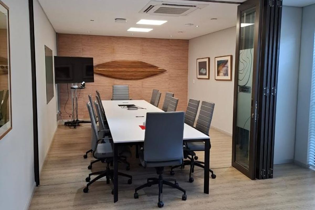 A professional office meeting room featuring a wood-look laminate floor, recessed ceiling lighting, ducted air conditioning, and a modern wood panel feature wall.