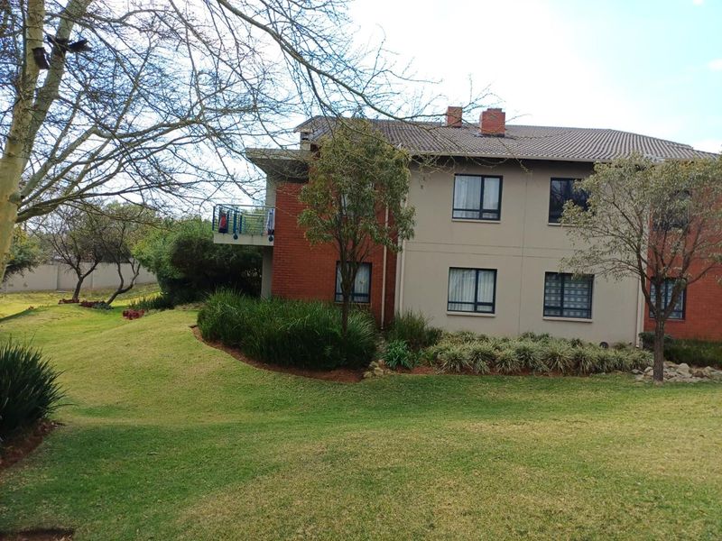 Rear view of the apartment building featuring a brick and plaster facade, tiled roof, and a private balcony overlooking a landscaped garden area.