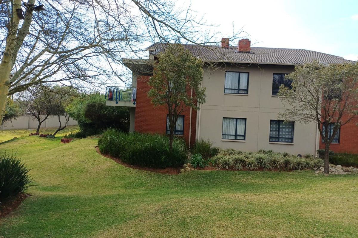Rear view of the apartment building featuring a brick and plaster facade, tiled roof, and a private balcony overlooking a landscaped garden area.