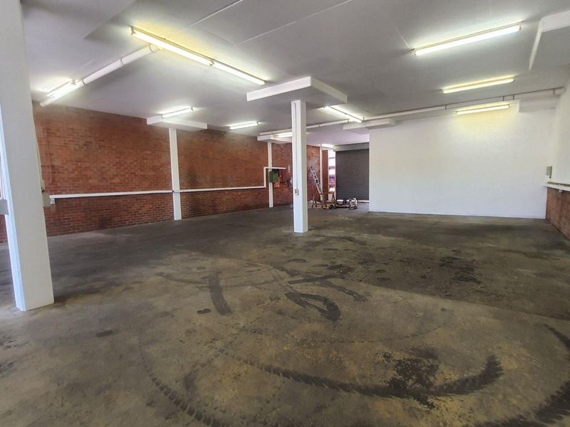 Spacious industrial utility area featuring exposed brick walls, concrete flooring, and high-clearance ceilings with fluorescent lighting, suitable for workshop or storage use.