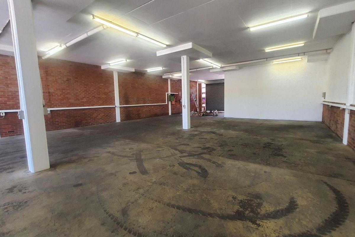 Spacious industrial utility area featuring exposed brick walls, concrete flooring, and high-clearance ceilings with fluorescent lighting, suitable for workshop or storage use.