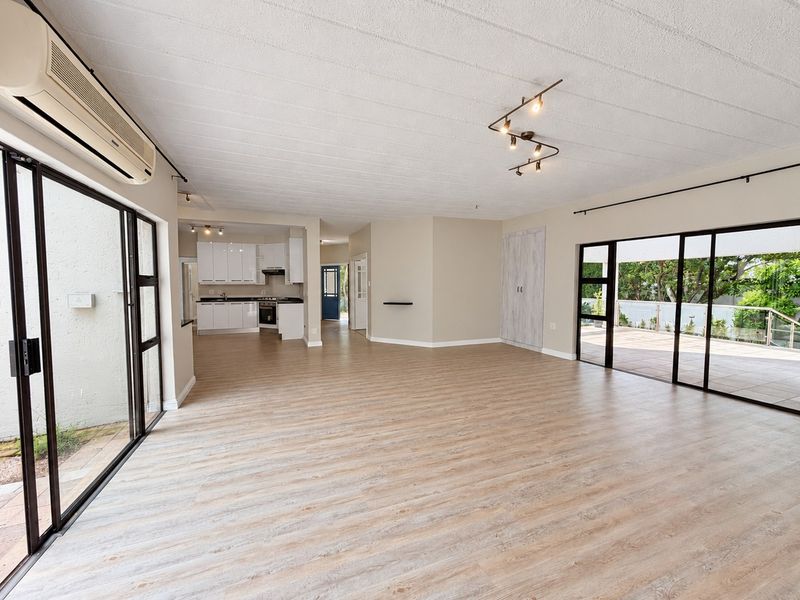 Spacious open-plan living area featuring modern laminate flooring, track lighting, split-system air conditioning, and seamless access to outdoor patio spaces.