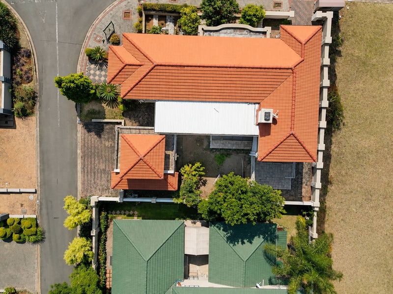 Aerial view of the property showcasing the terracotta tiled roof, perimeter wall, and paved driveway layout within the residential estate.
