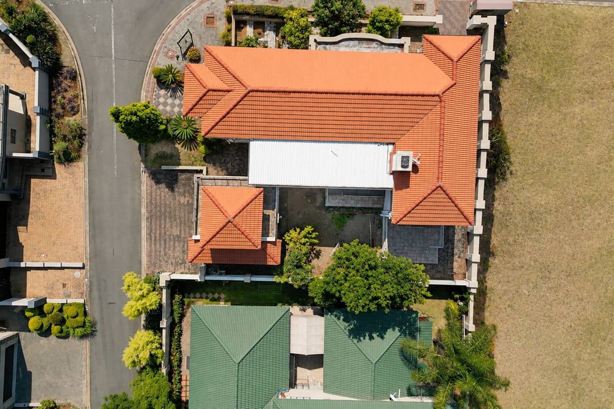 Aerial view of the property showcasing the terracotta tiled roof, perimeter wall, and paved driveway layout within the residential estate.