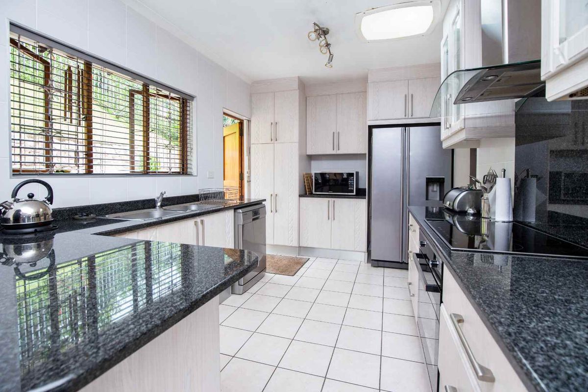 A functional kitchen featuring granite countertops, light-toned cabinetry, tiled flooring, and integrated appliances including a hob, oven, and extractor fan.