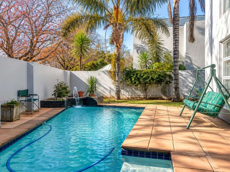 A private outdoor pool area featuring a built-in water feature, tiled surround, and established garden landscaping enclosed by high boundary walls.