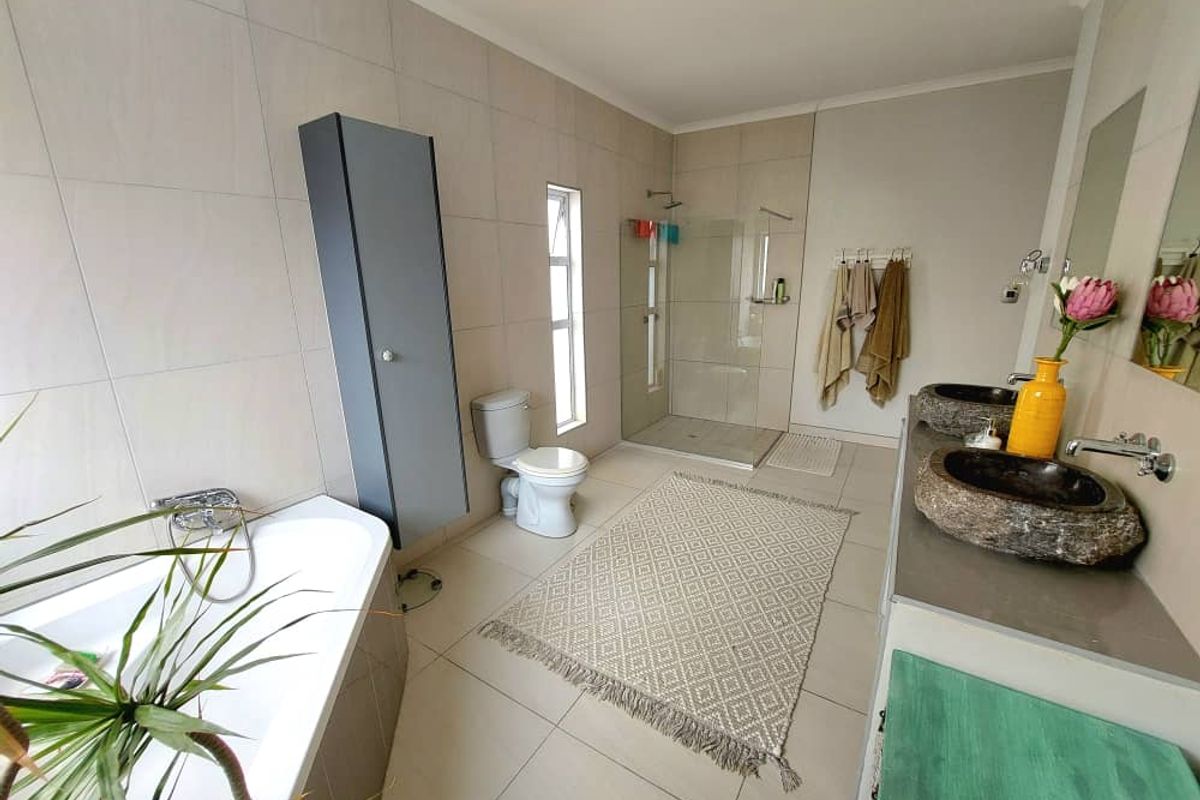 Spacious modern bathroom featuring a walk-in glass shower, a separate bathtub, and dual stone vessel sinks set on a vanity.