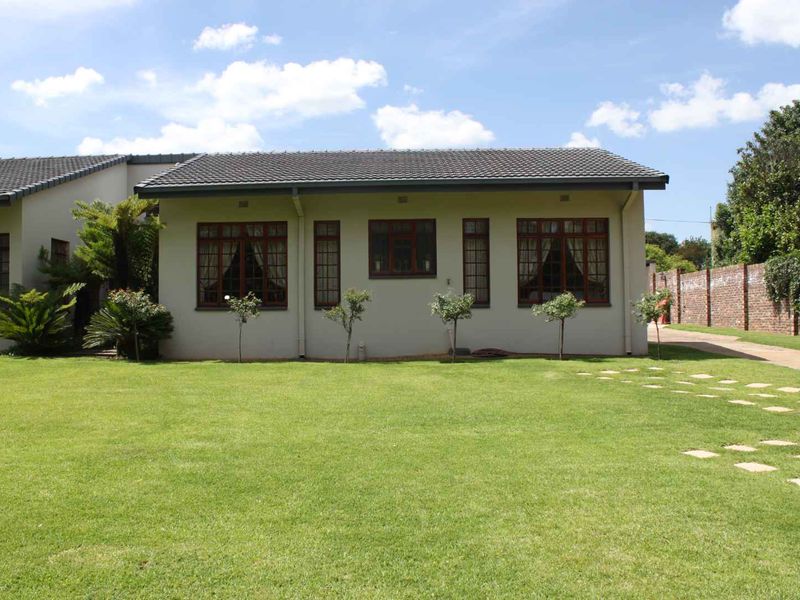 Rear view of the cottage featuring a well-maintained lawn, paved driveway, and brick boundary wall.