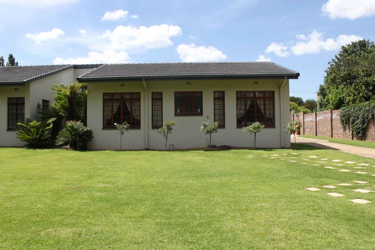 Rear view of the cottage featuring a well-maintained lawn, paved driveway, and brick boundary wall.