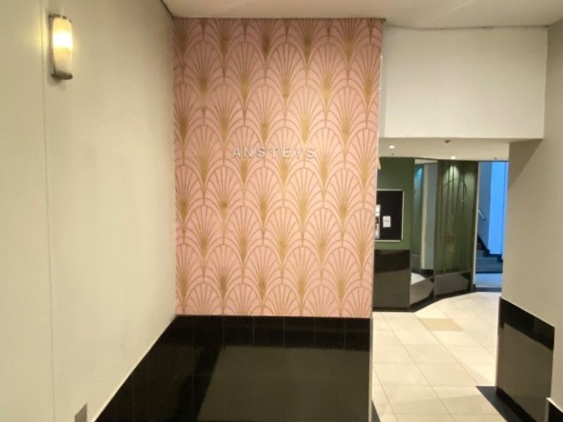 A clean and well-maintained apartment building entrance lobby featuring tiled flooring, decorative accent wallpaper, and modern recessed lighting.