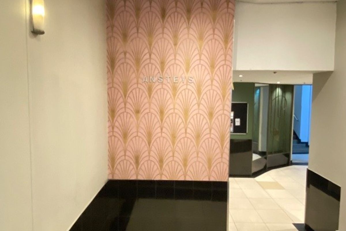 A clean and well-maintained apartment building entrance lobby featuring tiled flooring, decorative accent wallpaper, and modern recessed lighting.
