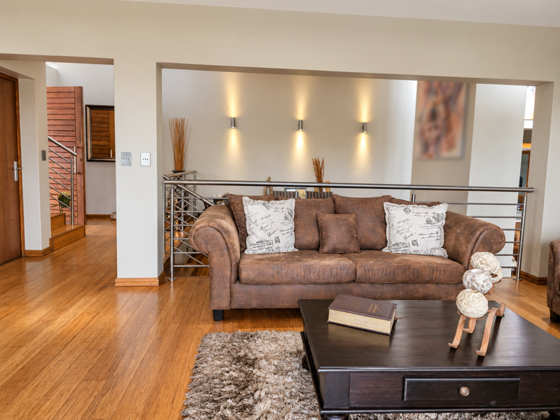 A well-maintained living area featuring warm hardwood flooring, a modern stainless steel balustrade, and elegant recessed wall lighting.