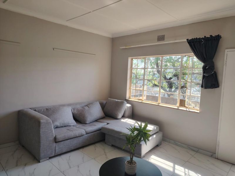 A living room featuring neutral wall tones, marble-look tiled flooring, and a large grid-pattern window allowing natural light.