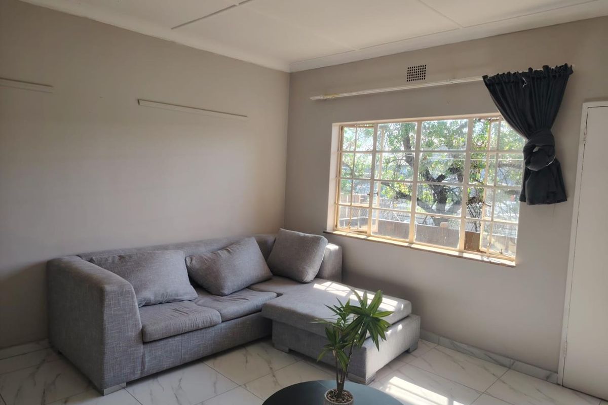 A living room featuring neutral wall tones, marble-look tiled flooring, and a large grid-pattern window allowing natural light.
