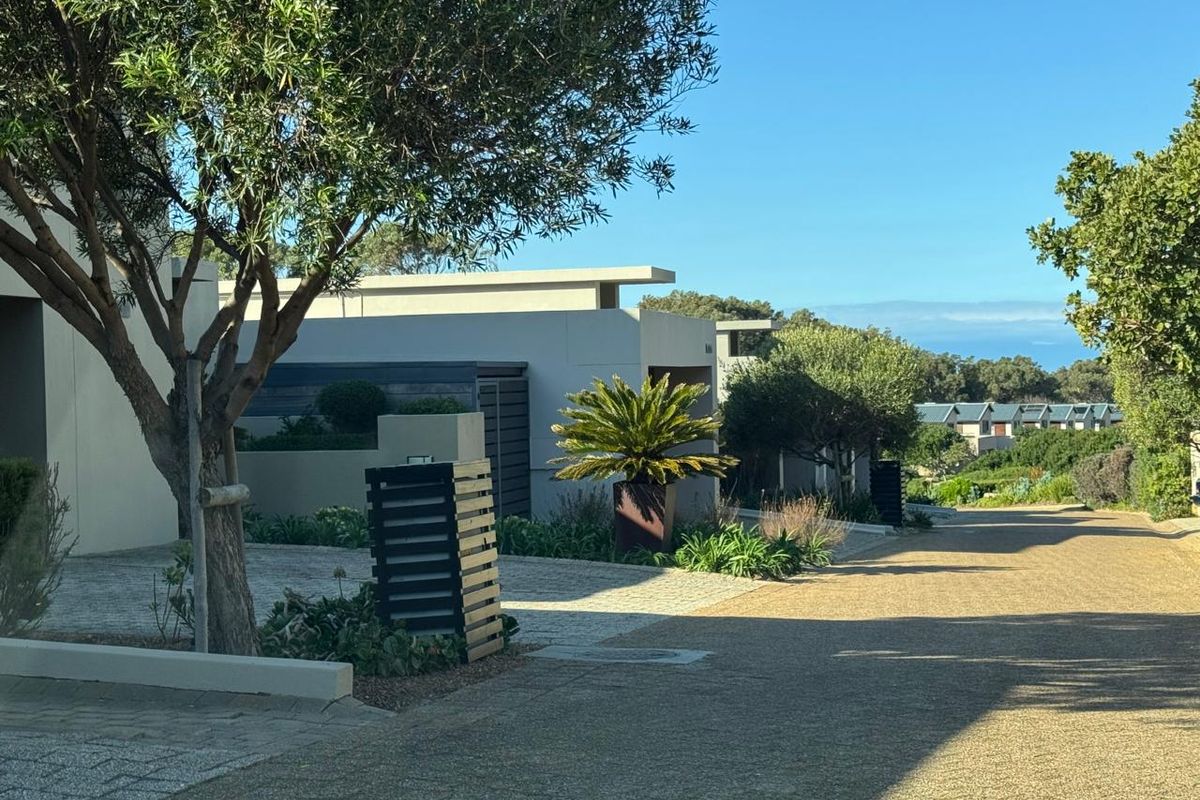 A view of the street approach featuring modern residential architecture, paved driveways, and well-maintained landscaped gardens in a coastal estate setting.