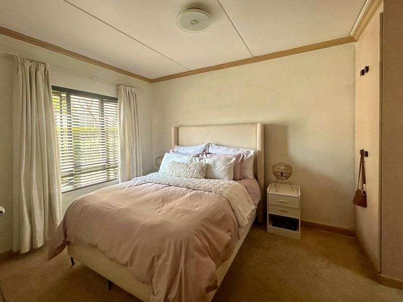 A cozy bedroom featuring a built-in wardrobe, carpeted flooring, and natural light through venetian blinds.