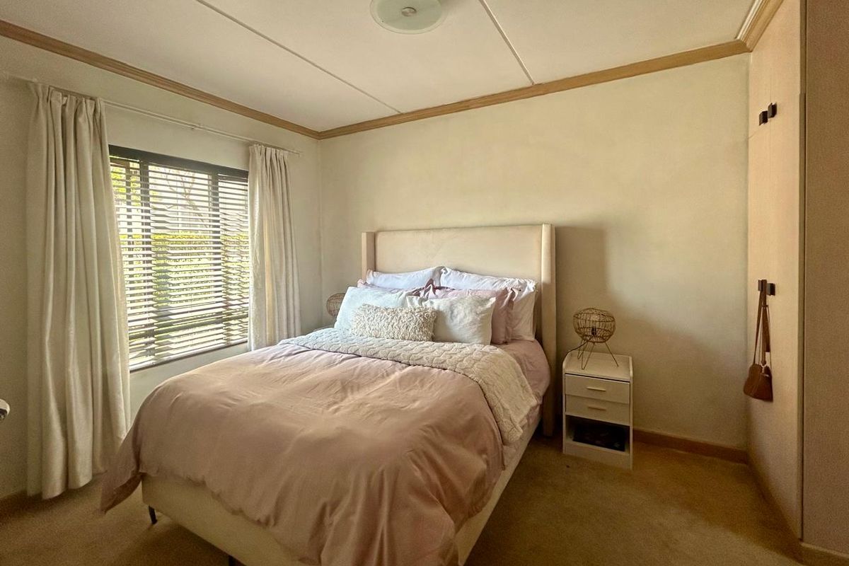 A cozy bedroom featuring a built-in wardrobe, carpeted flooring, and natural light through venetian blinds.