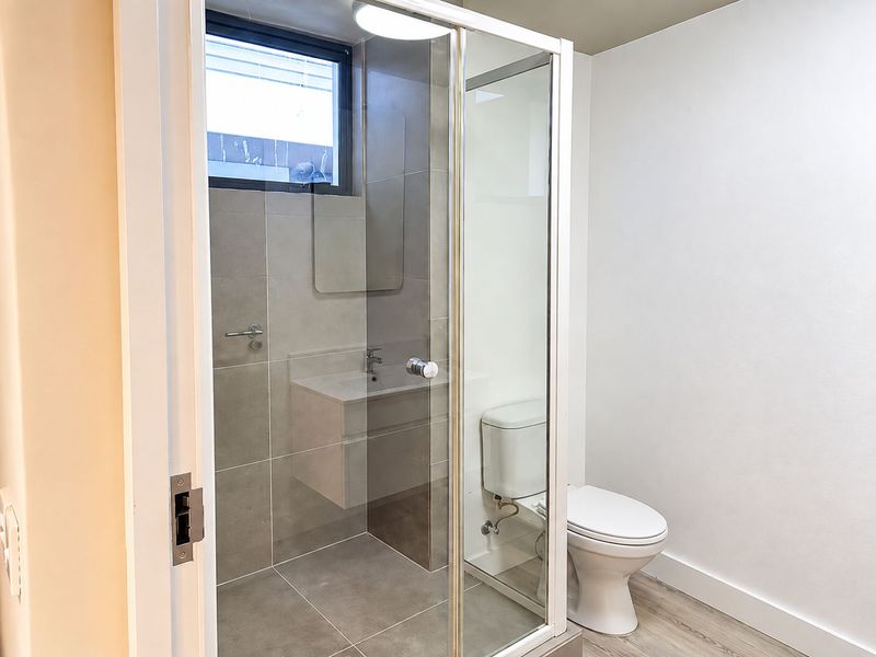 Modern bathroom featuring a glass-enclosed shower, wall-mounted vanity with basin, and a standard toilet, finished with neutral grey tiling.