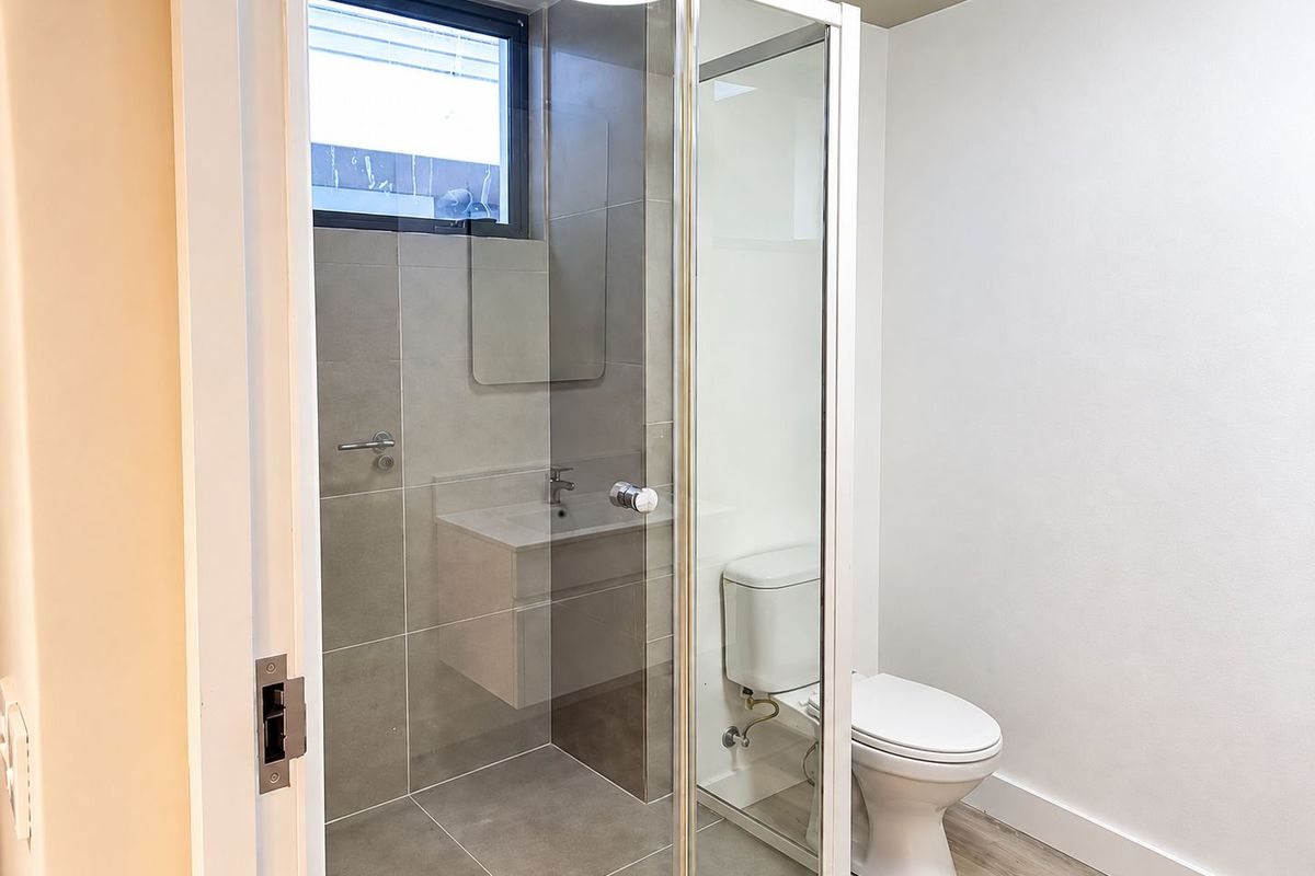 Modern bathroom featuring a glass-enclosed shower, wall-mounted vanity with basin, and a standard toilet, finished with neutral grey tiling.