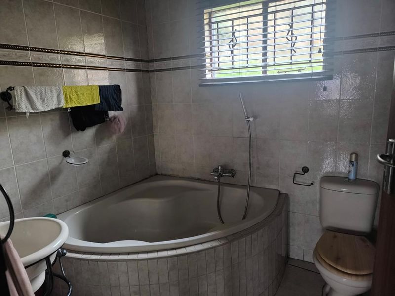 A functional bathroom featuring a corner bathtub with handheld shower attachment, tiled walls, and a standard toilet.