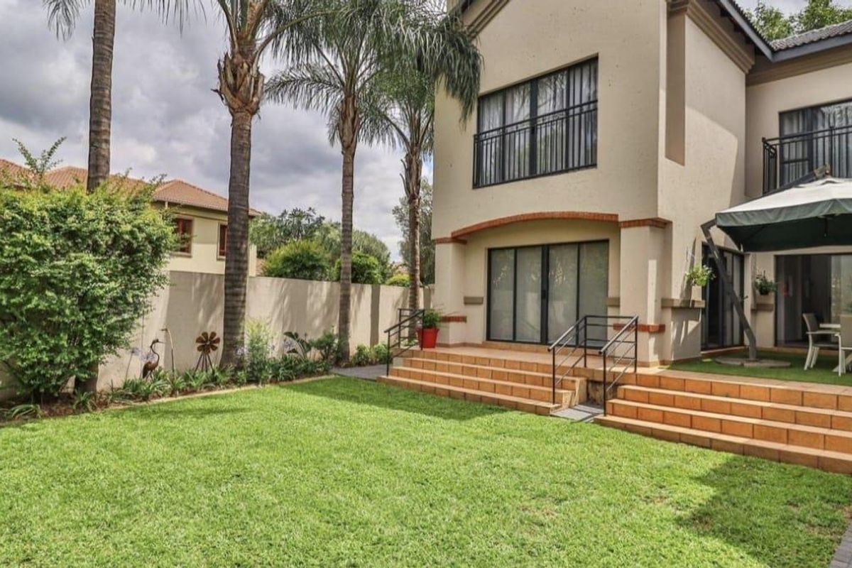 Rear view of the property featuring a tiled patio with steps, a well-maintained lawn, and a balcony overlooking the garden.
