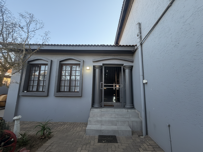 Rear exterior view featuring a paved patio, tiled entrance steps with decorative columns, and grid-style windows on a grey rendered facade.