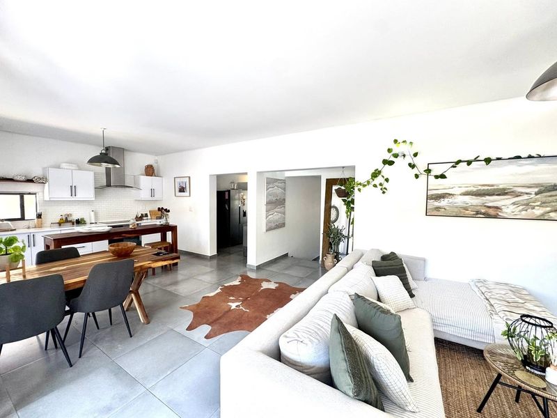 Spacious open-plan living and dining area featuring a modern kitchen with white cabinetry, subway tile backsplash, and large format floor tiles.