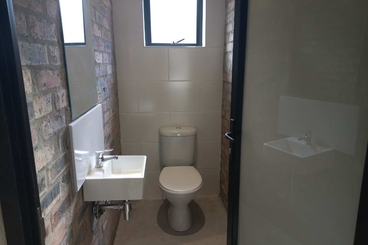 A compact guest bathroom featuring exposed brick walls, a wall-mounted basin, and a modern toilet.