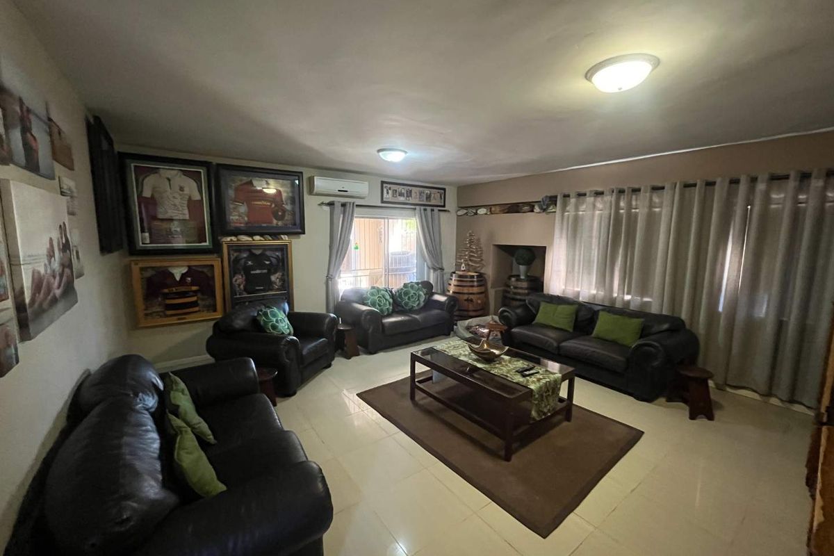 A spacious living room featuring tiled flooring, a wall-mounted air conditioning unit, and large windows with curtain treatments.