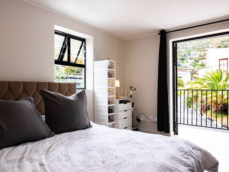 A bright bedroom featuring neutral walls, laminate flooring, and direct access to a private balcony through a glass door.