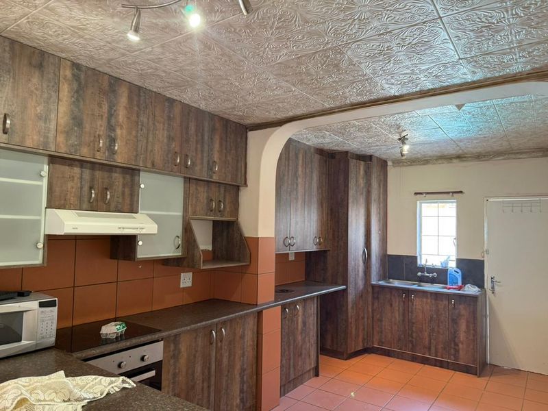 A functional kitchen featuring wood-look laminate cabinetry, built-in appliances, tiled splashbacks, and a distinctive textured ceiling finish.