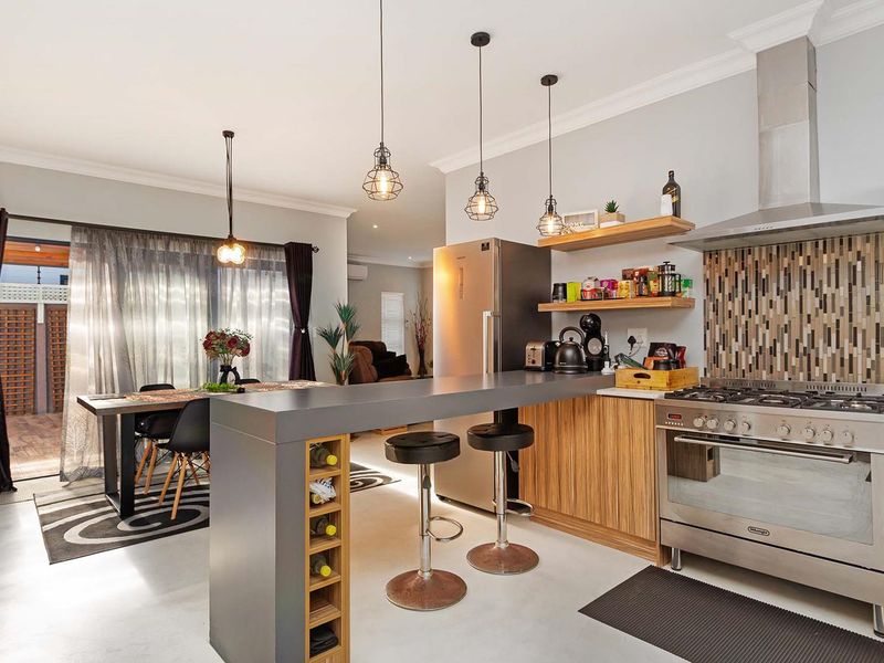 Modern open-plan kitchen and dining area featuring a gas stove, mosaic backsplash, breakfast bar with integrated wine storage, and direct access to the patio.