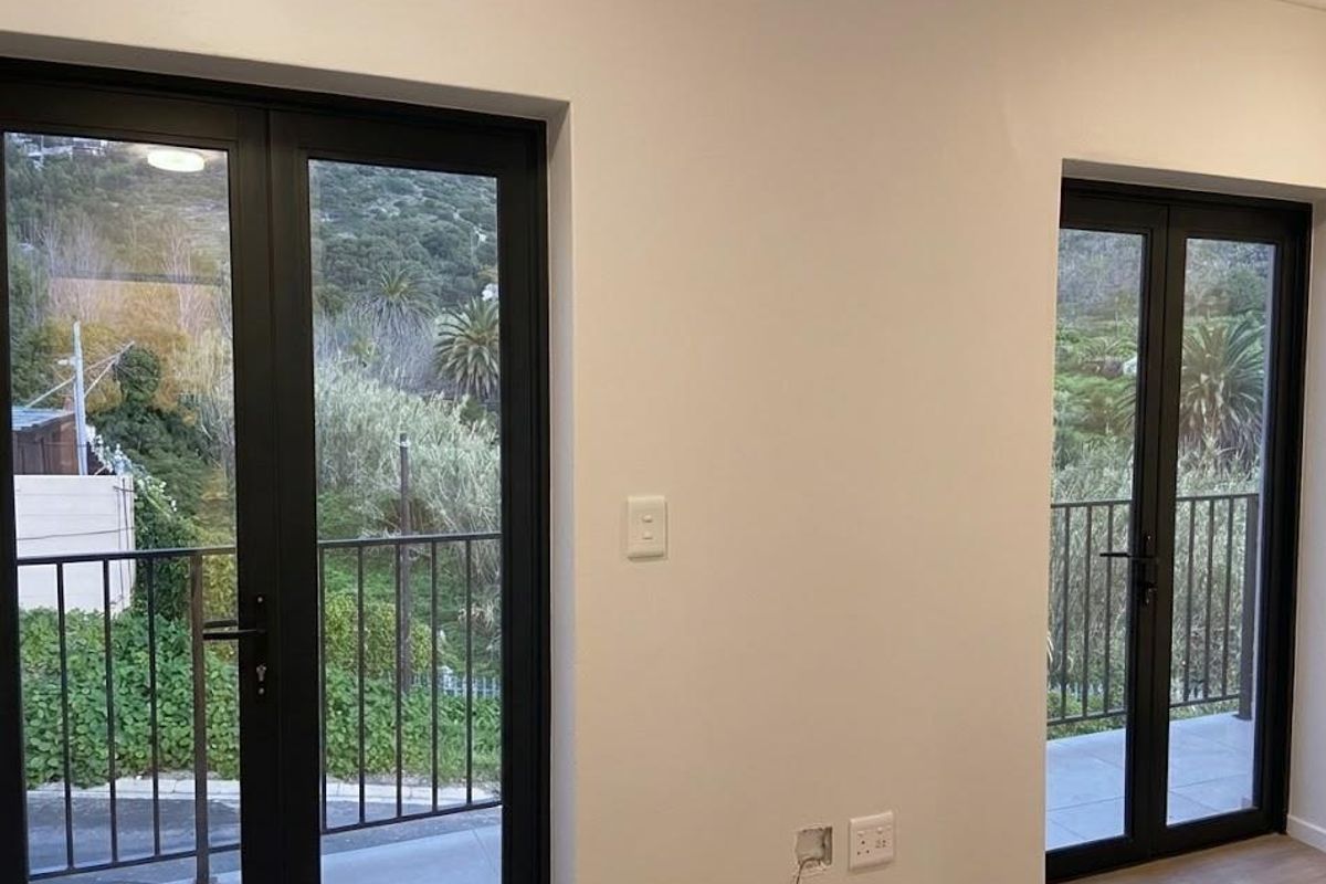 Bright living area featuring modern black-framed double doors opening onto a balcony with scenic hillside views.
